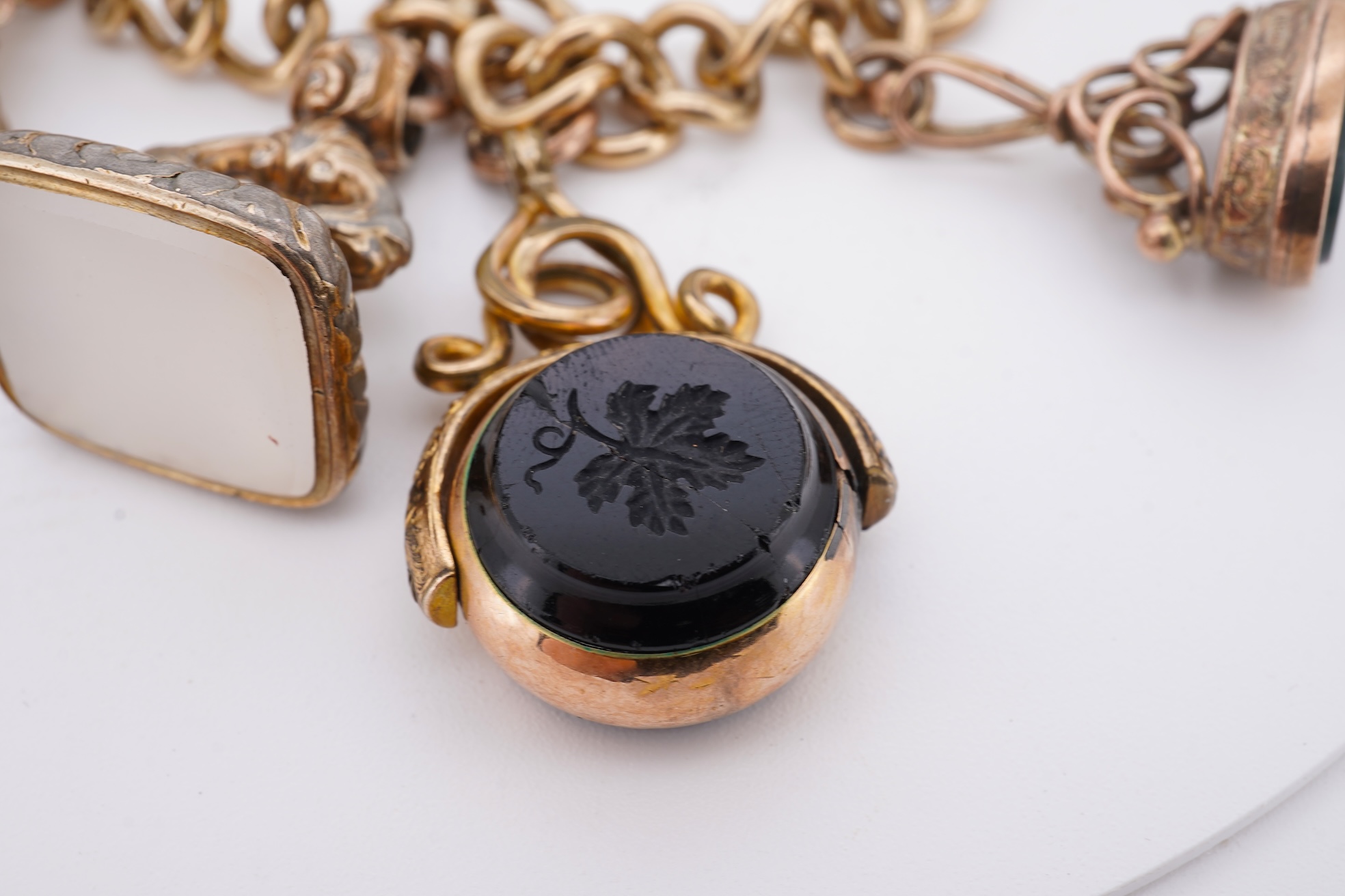 A 1970's 9ct gold curb link charm bracelet, with 9ct gold heart shaped clasp, hung with seven assorted gold or gilt metal mounted charms including six chalcedony set fob seals, gross weight 73 grams.